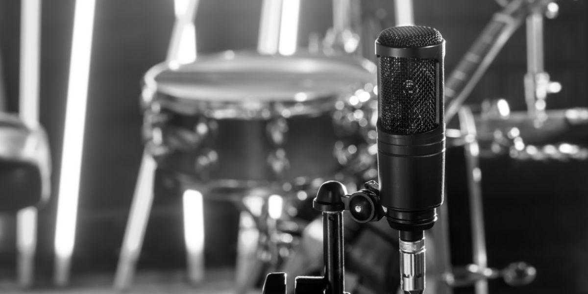 Condenser microphone in sharp focus with a drum kit in the background at a GoatHead Audio session