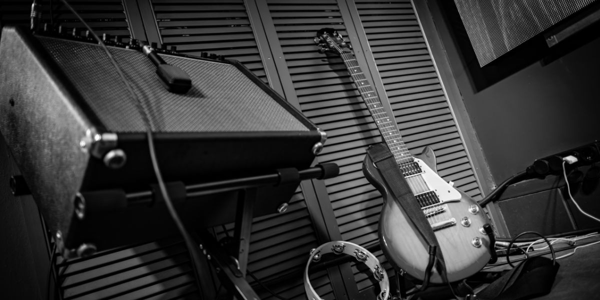 Electric guitar near amp with mic. Tambourine on floor, slatted doors. Guitar recording NM.