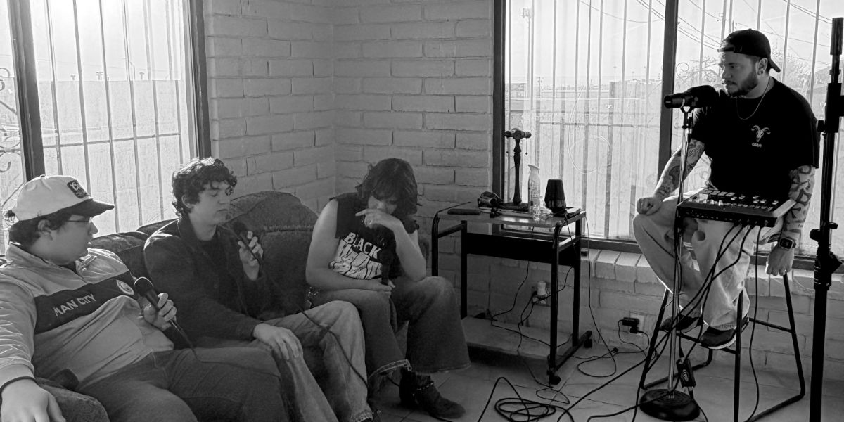 Podcast recording: group on couch, one at mic with mixer. Brick wall, sunlit room. NM.