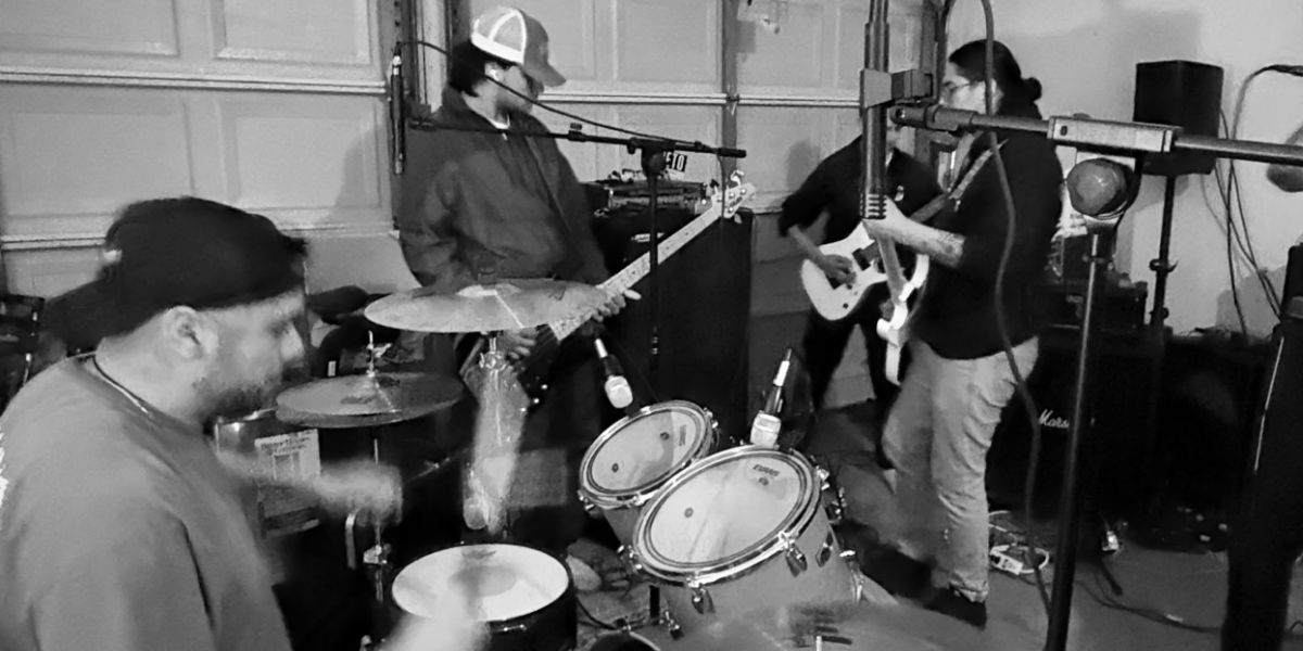 B&W band recording demo in garage - drummer, bassist, guitarist with mic stands, door visible